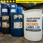 White container with Mzansi Label Lab adhesive label among blue barrels in a warehouse. Industrial Solvent & Chemical-Resistant Label Experts