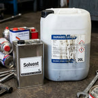 Two large containers of solvent on a workshop floor with tools around. Industrial Solvent & Chemical-Resistant Label Experts