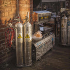 Two large gas cylinders with warning labels on a cart against a brick wall. Bakkie-Proof™ Industrial Gas &  Cylinder Labels 🏷️🔥
